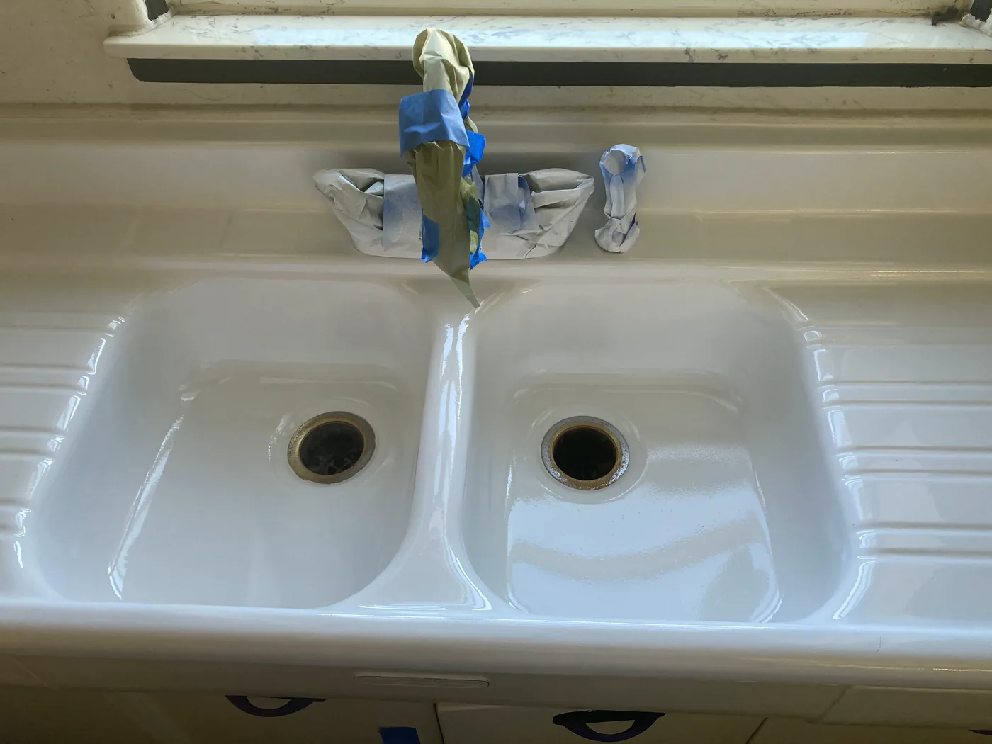 A double basin sink refinished in gloss white, faucet reinstalled.