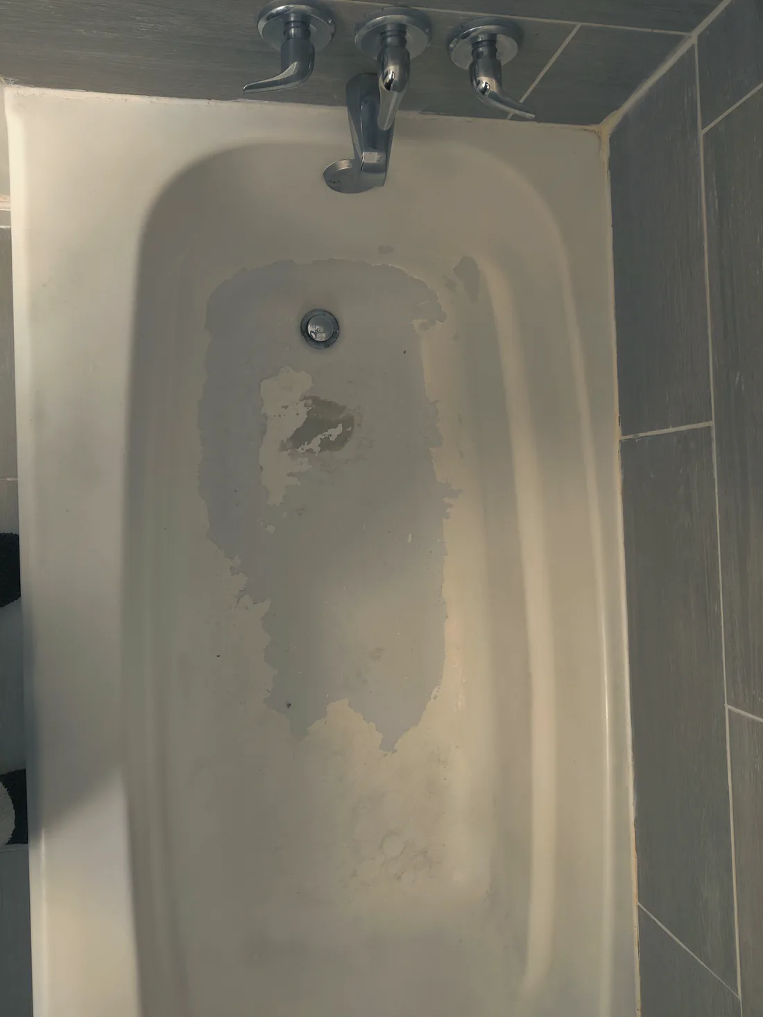 A gray bathtub with its finish flaking off in sheets.