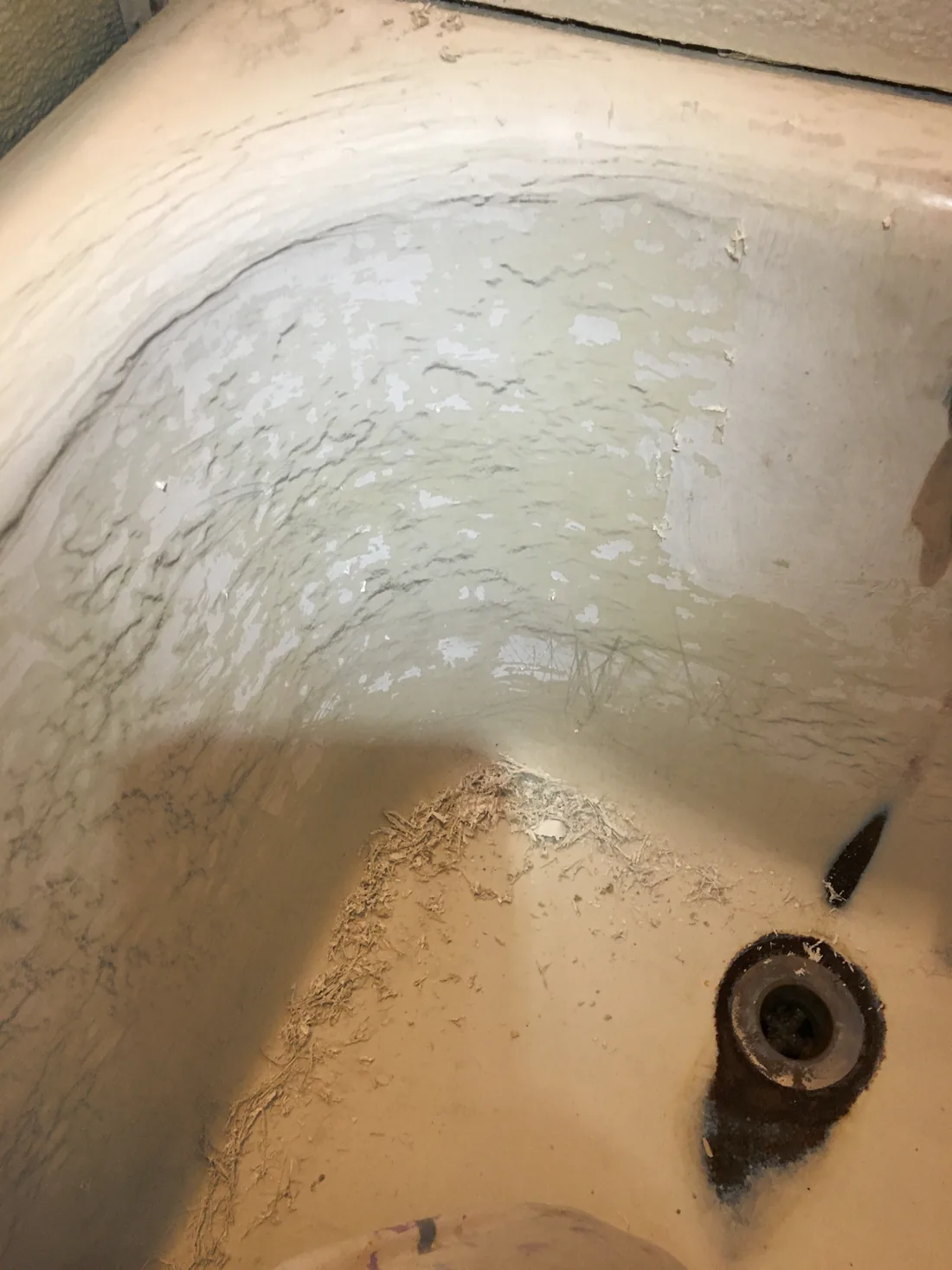 An old bathtub with the glaze peeling away around the drain.