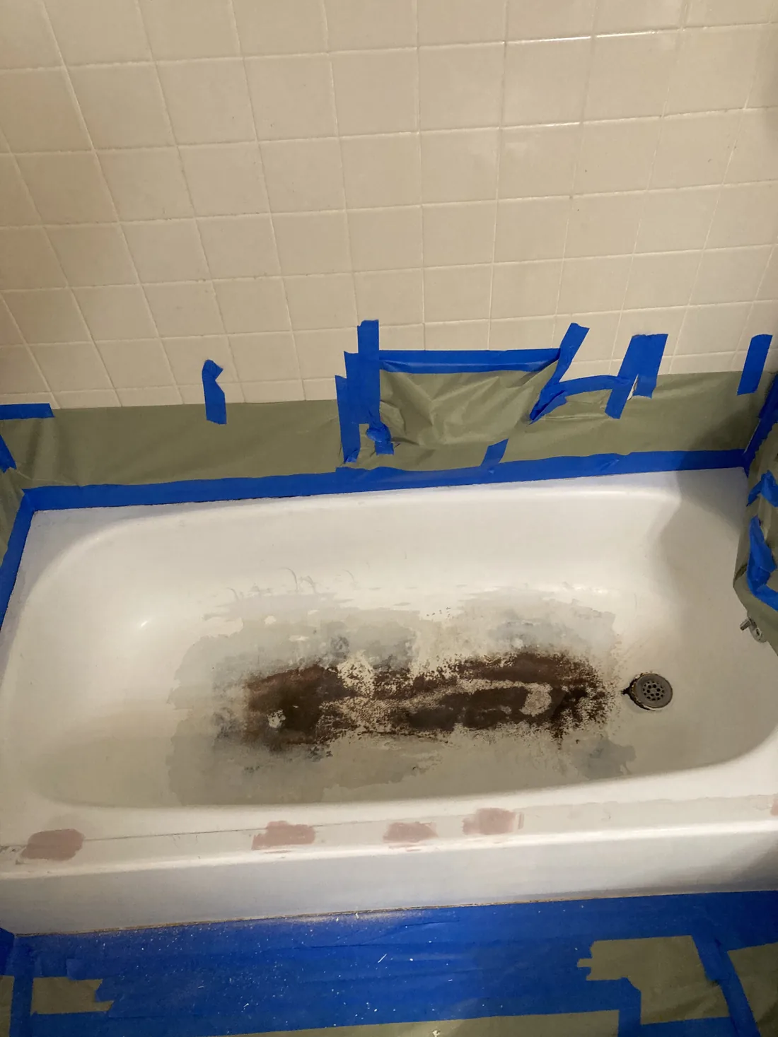 A bathtub masked off with blue tape, the basin rusted and worn through.