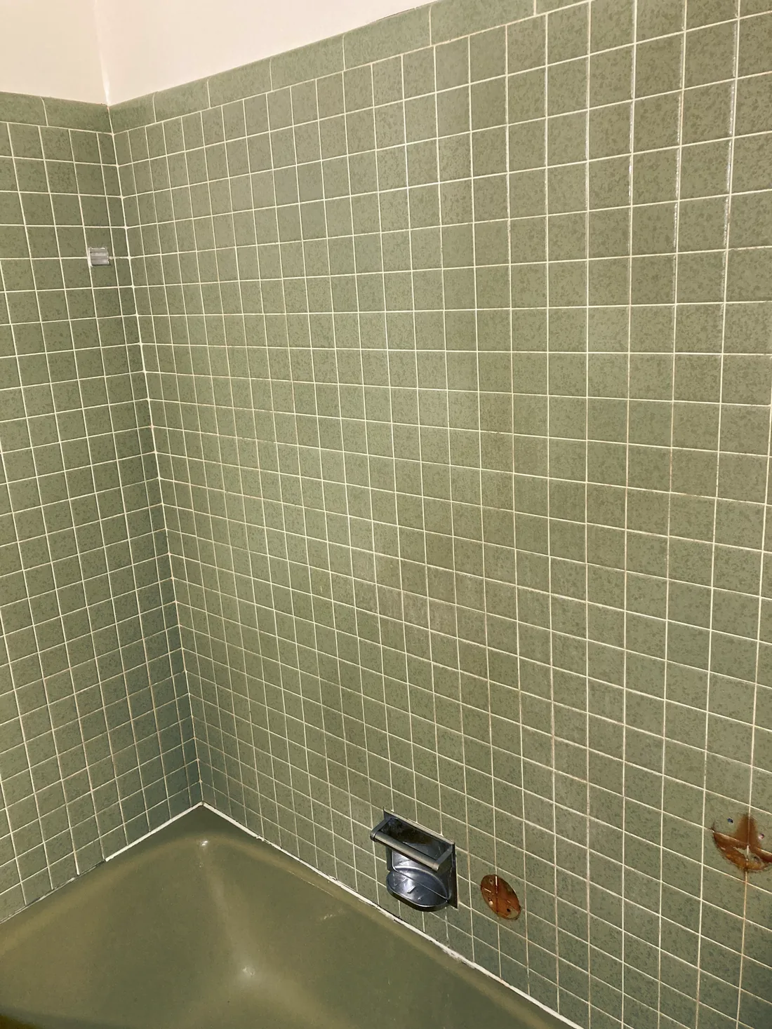 Avocado green wall tile around an old tub, before refinishing.